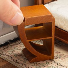 a hand is pointing at a small wooden shelf on the floor next to a bed