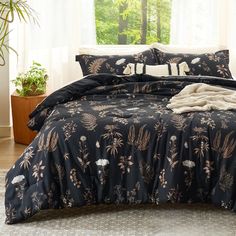 a bed covered in black and gold comforter next to a window with potted plants