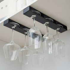 four wine glasses hanging from the ceiling in front of an overhead light fixture with three lights on each side