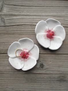 two white dishes with red flowers on them sitting on top of a wooden table next to each other