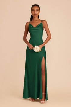 a woman in a long green dress standing with her hands on her hips and holding a bouquet