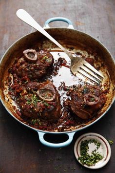 a pan filled with meat covered in sauce and vegetables next to a knife and fork