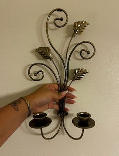 a hand holding a candle holder with three candles on it and two leaves attached to the wall