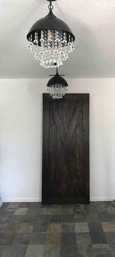 a chandelier hanging from the ceiling over a wooden door in a room with tile flooring