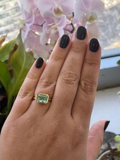 a woman's hand with black nails and a green ring