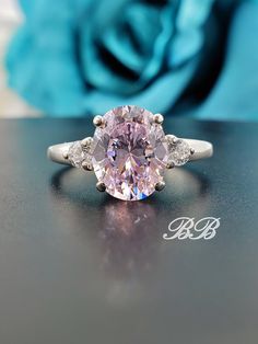 a pink diamond ring sitting on top of a black table next to a blue rose