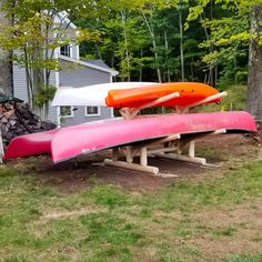 three canoes sitting on top of a wooden bench in front of a house and trees