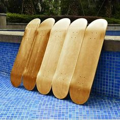 four skateboards are lined up against the edge of a swimming pool in front of a blue tiled wall