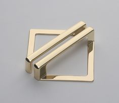 two metal square shaped objects on a gray surface, one is gold and the other is silver