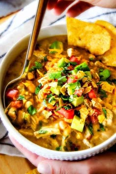 someone holding a bowl of mexican soup with tortilla chips