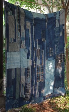 a blue quilt hanging from a clothes line in the woods with trees and grass behind it