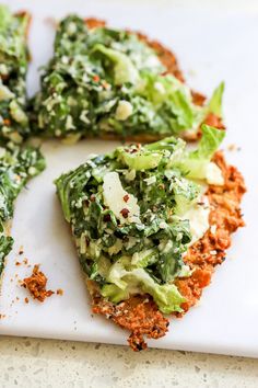 a white cutting board topped with slices of pizza covered in greens and seasoning sprinkles