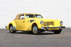 an old yellow car parked in front of a white brick wall