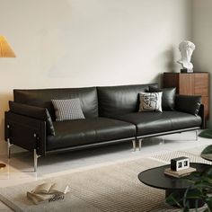 a black leather couch sitting in a living room next to a table and lamp on top of a rug