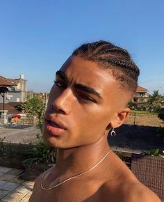 a young man with braids on his hair looks off into the distance while standing in front of a house