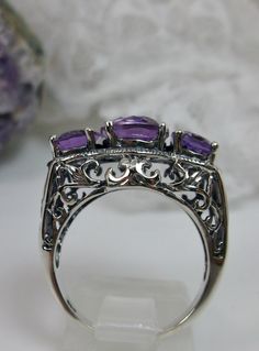 Natural Amethyst Ring 3Stone Design#36 Custom Made Inspired by Edwardian era designs, I now offer this exquisite reproduction ring in sterling silver. The full-cut natural amethyst in the center is 10mm (8/8th of an inch long), the 2 on the side are 8mm (5/16th of an inch long). The 3 stones together, east-west on the finger, are 20mm (13/16th of an inch) across. These flawless gemstones have perfect color and clarity. The band is hallmarked 925 for sterling. A ring gift-box is included. Feel fr Silver Amethyst Ring With Intricate Design, Oval Amethyst Ring With Intricate Design, Oval Purple Ring With Intricate Design, Purple Oval Ring With Intricate Design, Ornate Oval Amethyst Gemstone Ring, Oval Purple Amethyst Ring With Stone Setting, Purple Oval Filigree Ring For Anniversary, Purple Amethyst Rings With Intricate Design, Three Stone Amethyst Jewelry