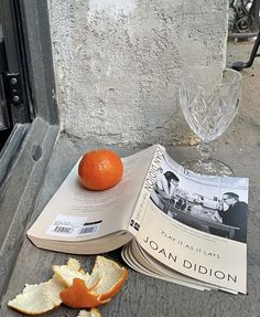 an orange sitting on top of a book next to a wine glass and magazine laying on the ground