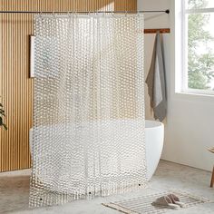 a white shower curtain in a bathroom next to a bathtub and window with wooden slats on the wall