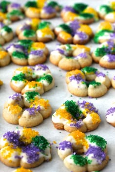 there are many decorated cookies on the baking sheet with purple, yellow and green sprinkles