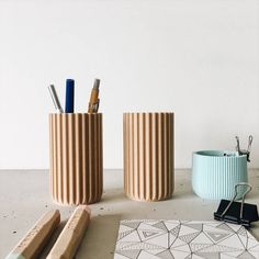 two vases sitting next to each other on top of a table with pens and pencils in them