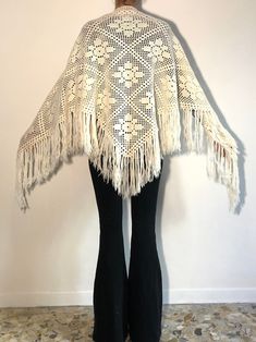 a woman wearing black pants and a white crocheted shawl with fringes