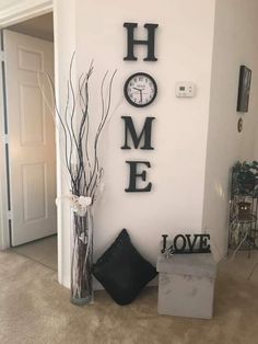 there is a clock on the wall next to a vase with branches in it and a sign that says home