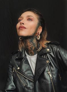 a woman with tattoos and piercings on her neck wearing a black leather biker jacket