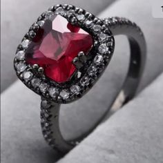 an engagement ring with a red stone surrounded by white and black diamonds on a gray surface