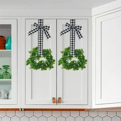 two wreaths with black and white bows on them are hanging from the cabinet doors