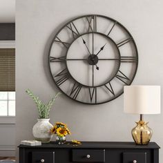 a large clock mounted to the side of a wall next to a table with flowers