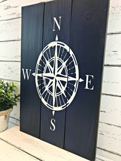 a wooden sign with a compass painted on it and a potted plant next to it