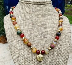 Nicely matched agate, carnelian, and jasper beads form a colorful choker necklace. A small brass African mask pendant is highlighted by bright gold-toned beads. Gold Carnelian Bohemian Beaded Necklace, Gold Carnelian Beaded Necklaces In Bohemian Style, Gold Carnelian Beaded Necklaces For Healing, Gold Carnelian Beaded Necklace In Bohemian Style, Gold Carnelian Beaded Necklace For Healing, Bohemian Gold Beaded Carnelian Necklaces, Gold Bohemian Beaded Carnelian Necklaces, Colorful Choker, Marble Falls