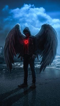 a man standing on the beach with an angel wings back lite up in front of him