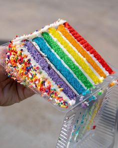 a hand holding a slice of rainbow cake