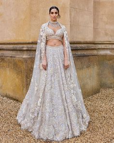 This lehenga set features three-dimensional embroidery in a bold floral pattern in thread, pearl, sequin and beads. The blouse has a plunging neckline and shows exaggerated pearl tassels. It is paired with a matching four sided embroidered dupatta. It is paired with an optional embroidered organza cape with a trail at the back.From Seema Gujral's A Royal Affair collection. DELIVERY TIMEPlease allow 8-12 weeks for your outfit to arrive. FABRIC DETAILSNet Professional cleaning only. Cream Hand Embellished Lehenga For Reception, Hand Embellished Cream Lehenga For Reception, Glamorous Floral Embroidered Sets For Reception, Glamorous Sets With Floral Embroidery For Reception, Glamorous White Choli With Traditional Drape, Glamorous White Choli For Reception, Glamorous Floral Embroidery Wedding Sets, Glamorous Wedding Sets With Floral Embroidery, Glamorous White Hand Embellished Lehenga