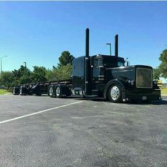 a black semi truck parked in a parking lot next to some trees and blue sky