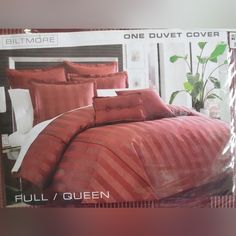 a bed with red sheets and pillows in a box on the floor next to a plant