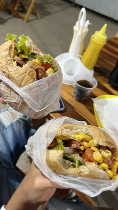 two people holding sandwiches in their hands at a table with other food items on it