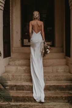 a woman in a white dress is walking up some steps with her back to the camera