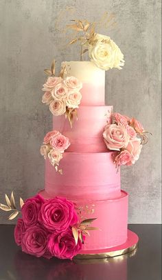 a three tiered cake with pink and white flowers on the top, sitting on a table