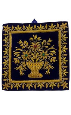 a blue and gold embroidered wall hanging with an image of a vase in the center