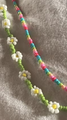 a multicolored beaded necklace is laying on a gray shirt with white and yellow flowers