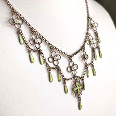 This antique silver and green and white enamel necklace was hand crated in the Arts and Crafts era, around 1910 by famed Norwegian silver smith Marius Hammer. Hammer lived from 1847-1927 and worked in Bergen, Norway. This drop necklace features flowers and drops of bright spring green and matte what enamel with that velvety look that Hammer was a master of. Chains of silver weave throughout this necklace, piecing together a lovely statement piece of swirls, loops, and twists. This piece weighs 10.3 grams and measures 16 inches in length. It has been acid tested. A mark on the back reads, ‘930S’, indicating fine silver and it bears the hallmark of the M with a hammer forming the center.  Wearable on a Saturday night date, give-able for a wedding present, presentable at a cocktail party, and Antique Enamel Pendant Jewelry, Antique Enamel Necklace Hallmarked, Antique Enamel Necklace With Hallmark, Antique Enamel Hallmarked Necklaces, Victorian Gold Enamel Necklace, Victorian Enamel Pendant Jewelry, Victorian Round Enamel Jewelry, Formal Art Nouveau Necklace, Art Deco Hallmarked Enamel Jewelry