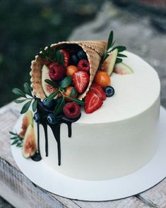 a white cake topped with fruit and chocolate drips on top of a wooden table