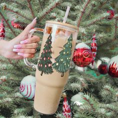 a woman holding a coffee cup in front of a christmas tree with ornaments on it