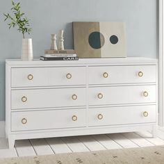 a white dresser with gold handles and knobs in a blue room next to a potted plant