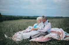 an older couple sitting on a blanket in a field