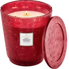 a large red candle with a lid on it's side and an ornate design in the middle