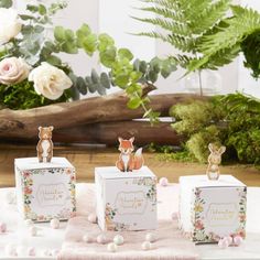 three small boxes with animals on them sitting on a table next to flowers and greenery