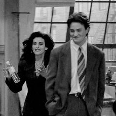 black and white photograph of man and woman walking down the street with drinks in their hands